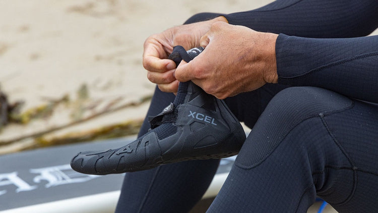 Surfer putting on a pair of Xcel surf booties.