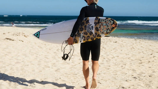 A surfer walking towards the ocean carrying his surfboard and leash.