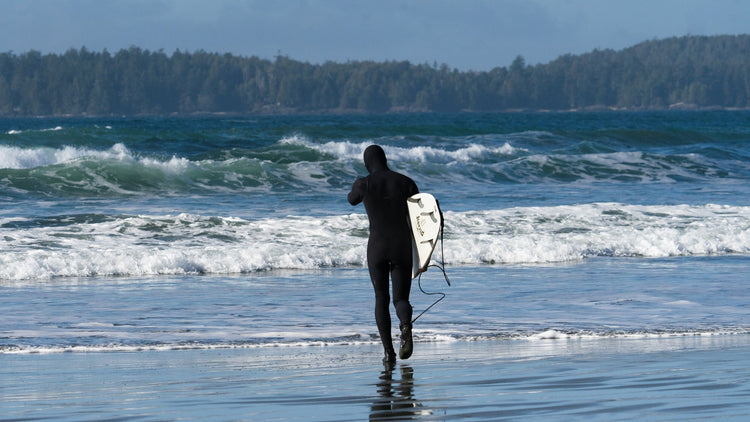 Surfer wearing a good fitting wetsuit walking out to the ocean while carrying his surfboard.